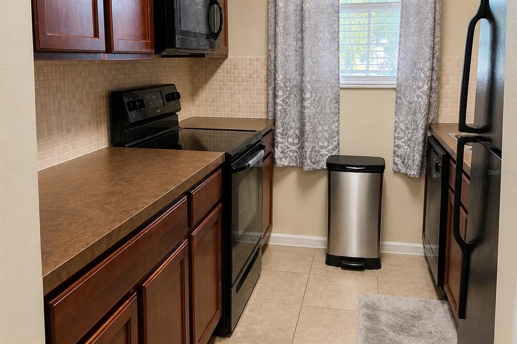 A galley kitchen features dark wood cabinets, black appliances, tan countertops, and a tiled backsplash — 4756 TANGERINE AVENUE UNIT 4756, WINTER PARK, FL