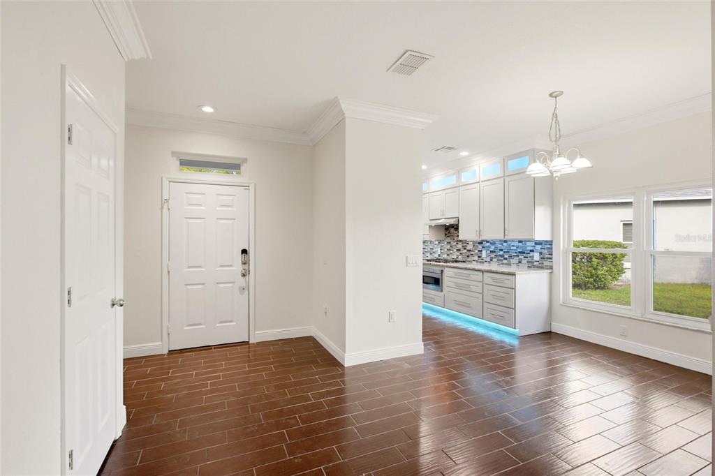 A bright entryway leads into a kitchen with white cabinets, blue backsplash, and tile flooring — 12347 HOLLYBUSH TERRACE, BRADENTON, FL