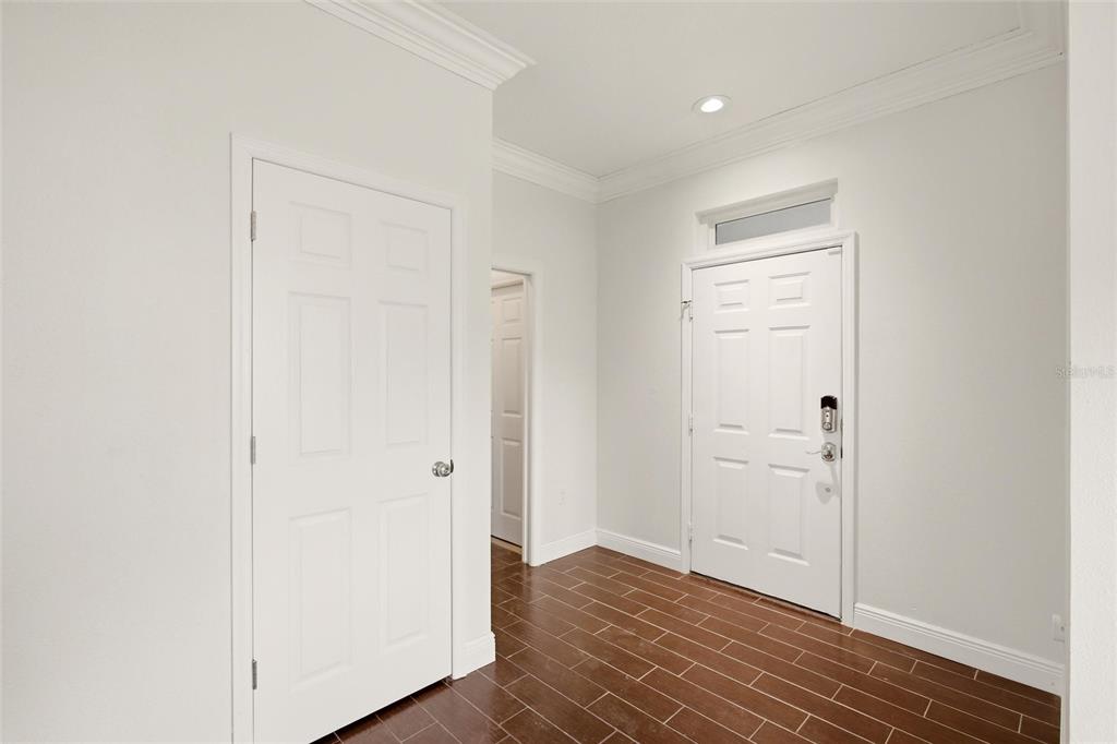 An entryway features white walls, crown molding, a white door, and dark wood-look tile flooring — 12347 HOLLYBUSH TERRACE, BRADENTON, FL