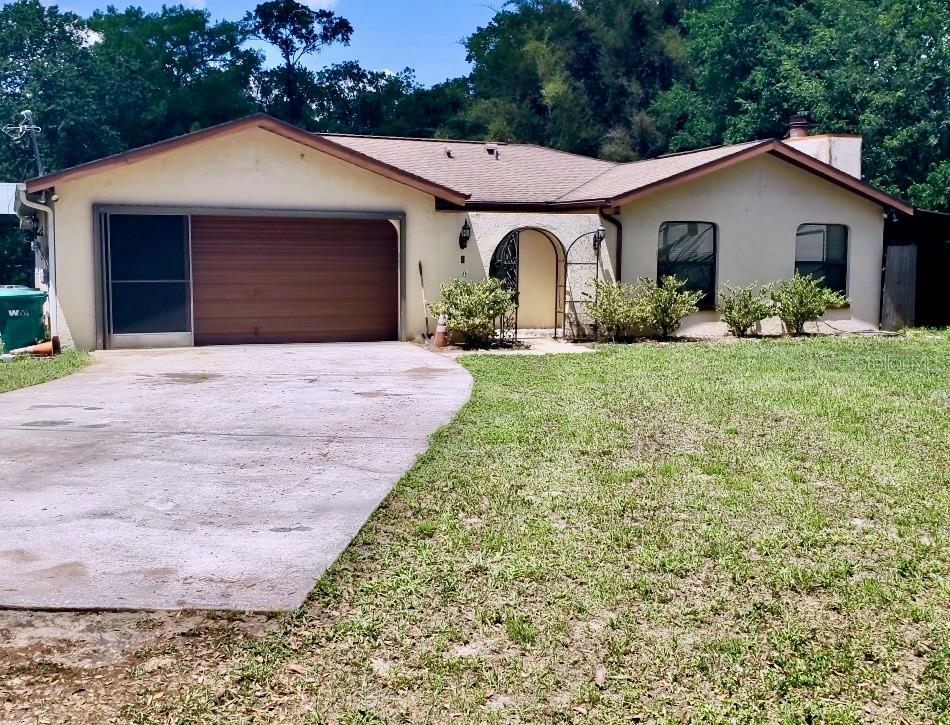 A single-story house with a garage, concrete driveway, and arched entryway surrounded by trees — 490 S MINSTREL AVENUE, INVERNESS, FL