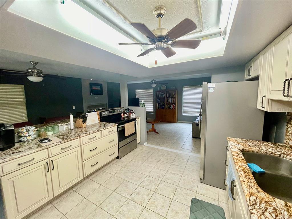A kitchen with cream cabinets, granite countertops, and a ceiling fan in a recessed tray — 490 S MINSTREL AVENUE, INVERNESS, FL