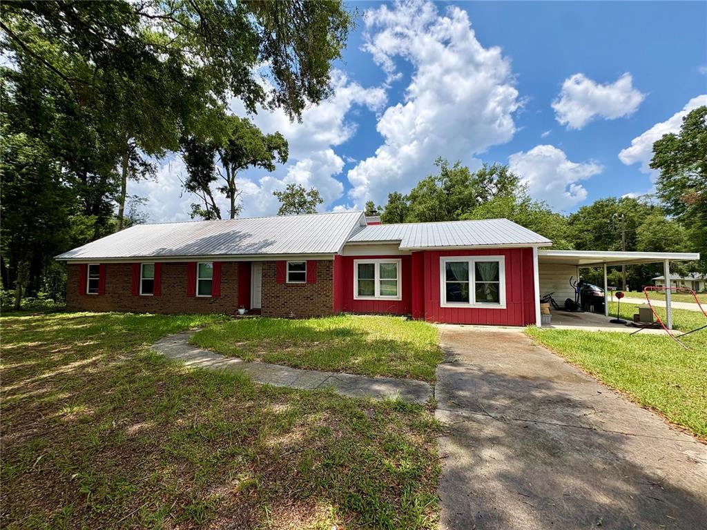 A single-story house with a metal roof, red siding, brick facade, and an attached carport — 507 GOVERNOR AVENUE NE, BRANFORD, FL
