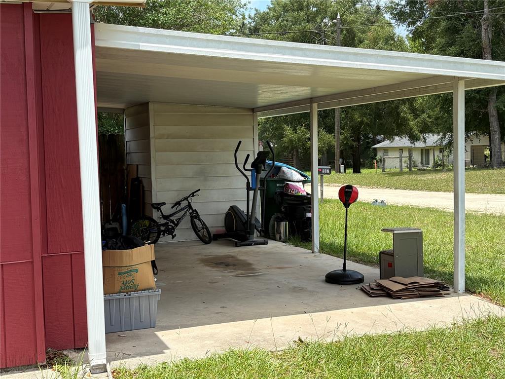 A covered concrete carport features a bicycle, an elliptical machine, and a punching bag — 507 GOVERNOR AVENUE NE, BRANFORD, FL