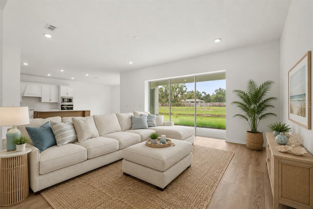 A living room with a large sectional sofa, sliding glass doors, and a kitchen background — 12105 ORCHID ASH STREET, RIVERVIEW, FL