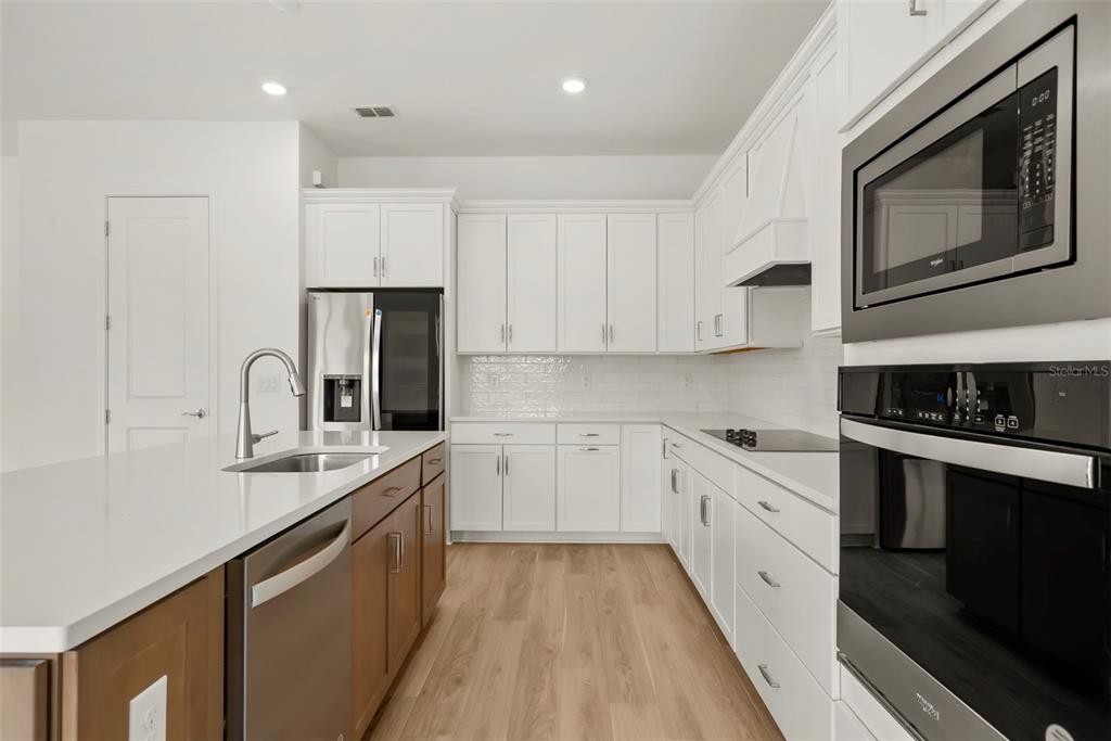 A modern kitchen features white cabinets, stainless steel appliances, a center island, and wood flooring — 12105 ORCHID ASH STREET, RIVERVIEW, FL