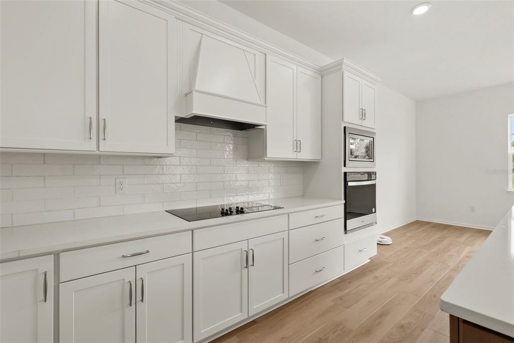 A modern kitchen features white cabinetry, a subway tile backsplash, and stainless steel built-in ovens — 12105 ORCHID ASH STREET, RIVERVIEW, FL