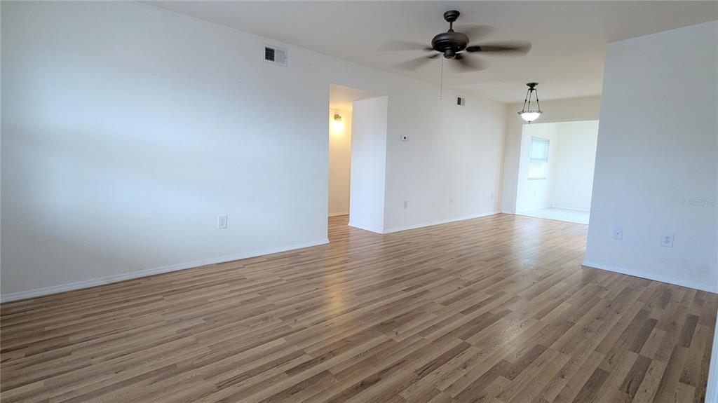 An empty living area features light wood-look flooring, white walls, and a ceiling fan — 4158 TAMIAMI TRAIL UNIT U3, PORT CHARLOTTE, FL