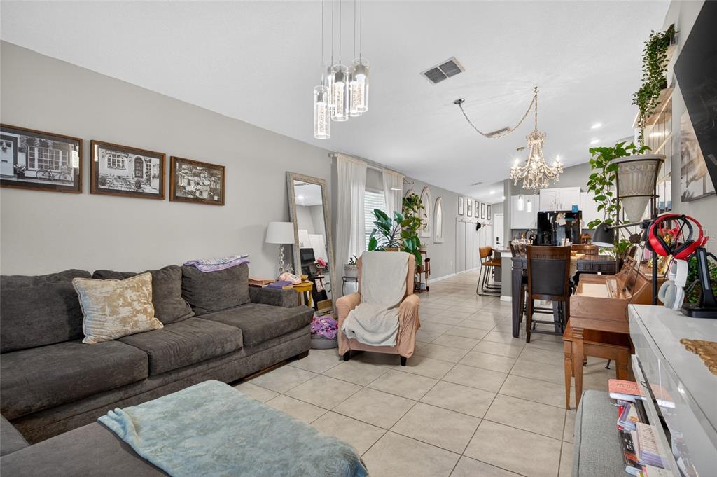 An open-concept living room and kitchen area features tile flooring, a chandelier, and neutral walls — 3915 GAINER SPRINGS AVENUE, NEW PORT RICHEY, FL