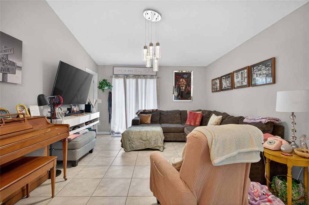 A living room features a sectional sofa, a piano, a television, and tile flooring — 3915 GAINER SPRINGS AVENUE, NEW PORT RICHEY, FL
