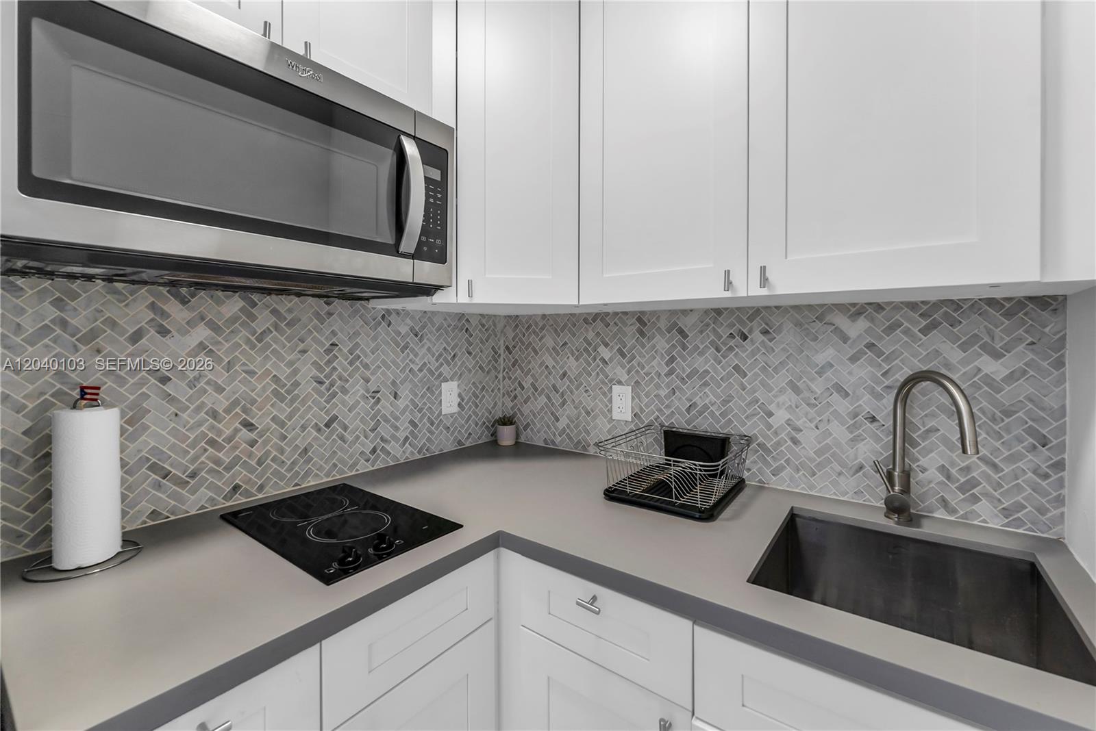 A kitchen features white cabinets, a grey countertop, a herringbone backsplash, and stainless steel appliances — 6647 SW 59th Pl # 208, South Miami FL 33143, SOUTH MIAMI, FL
