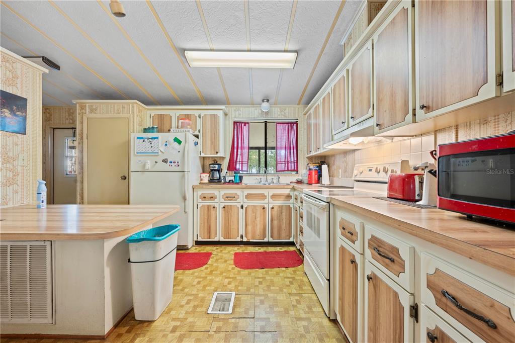 A kitchen features wood-trimmed cabinets, a white refrigerator, a red microwave, and patterned vinyl flooring — 7373 FALL STREET, BROOKSVILLE, FL