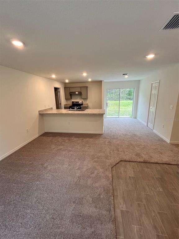 An open-concept living area features carpeted flooring, a kitchen with a breakfast bar, and sliding doors — 10300 RUTH AVENUE, HASTINGS, FL