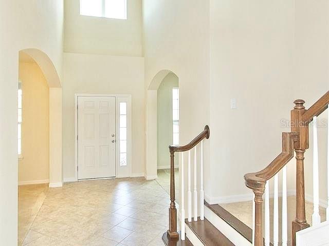 An entryway features a tiled floor, a high ceiling, and a wooden staircase with railings — 2103 CANDLENUT CIRCLE, APOPKA, FL