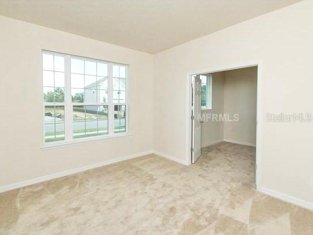 An empty room with beige carpet, a large window, and an open doorway — 2103 CANDLENUT CIRCLE, APOPKA, FL