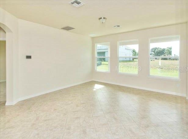 An empty room with beige tile flooring and three large windows overlooking a grassy yard — 2103 CANDLENUT CIRCLE, APOPKA, FL