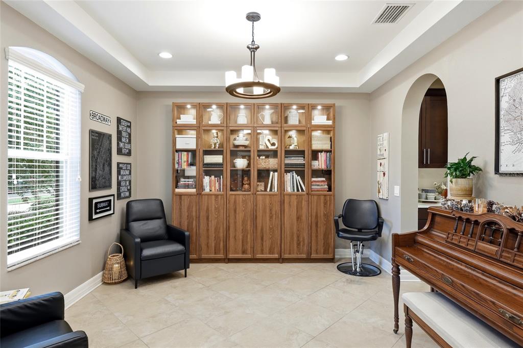 A room with tile floors, a large wooden bookcase, a piano, and a black armchair — 4446 WILDSTAR CIRCLE, WESLEY CHAPEL, FL