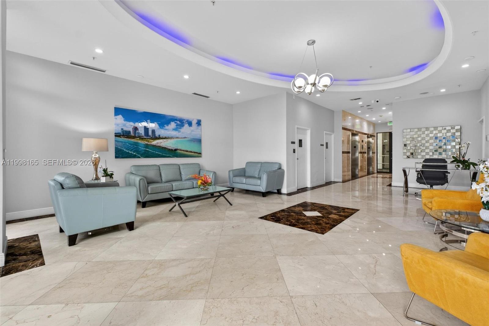 A modern building lobby features light-colored tile floors, blue and yellow seating, and recessed lighting — 2301 SW 27th Ave # 906, Miami FL 33145, MIAMI, FL