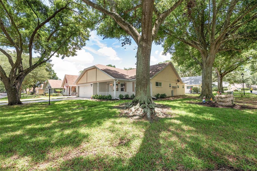 A single-story house with a light-colored exterior sits on a grassy lot under large trees — 8560 SW 90TH STREET UNIT E, OCALA, FL
