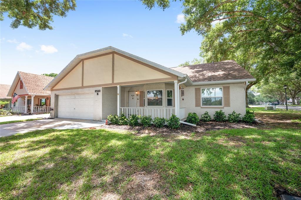 A single-story house with a white brick exterior, a two-car garage, and a front porch — 8560 SW 90TH STREET UNIT E, OCALA, FL