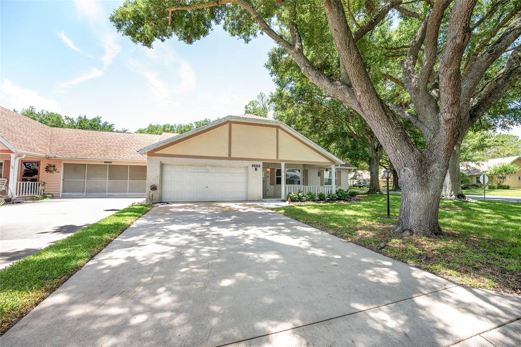 A single-story house with a white garage door, tan siding, and a large shade tree — 8560 SW 90TH STREET UNIT E, OCALA, FL
