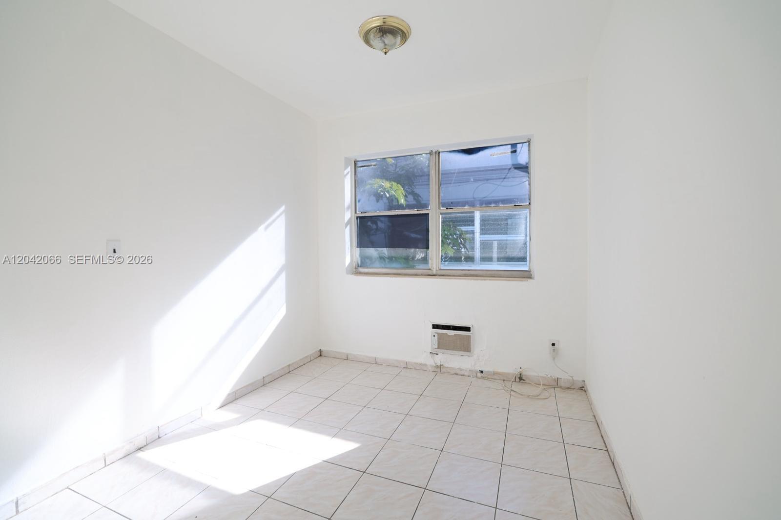 An empty room features white walls, light-colored tile flooring, a window, and a wall-mounted air conditioner — 770 83rd St # 3, Miami Beach FL 33141, MIAMI BEACH, FL