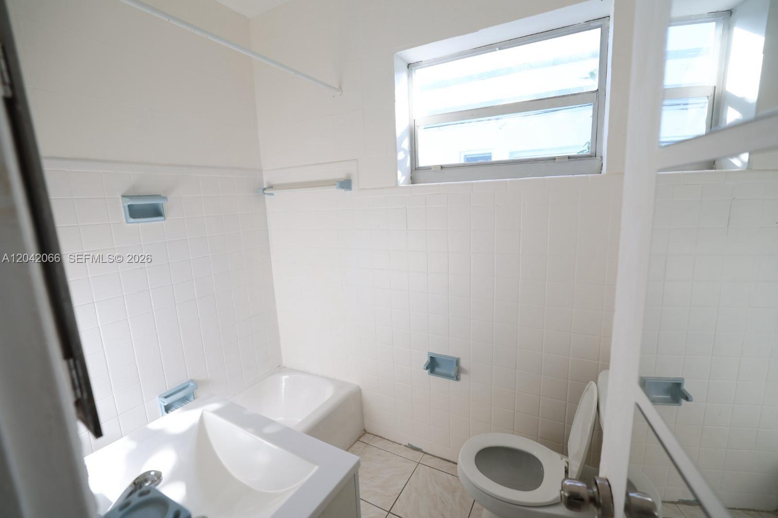 A bathroom features white tiled walls, a bathtub, a toilet, and a window — 770 83rd St # 3, Miami Beach FL 33141, MIAMI BEACH, FL
