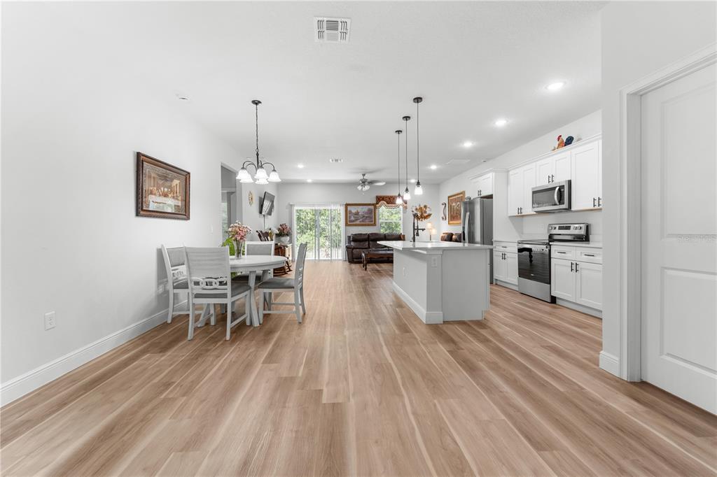 An open-concept kitchen and dining area features white cabinetry, a center island, and wood flooring — 768 MARION OAKS MANOR, OCALA, FL