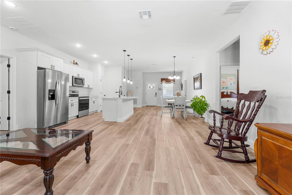An open-concept kitchen and dining area features white cabinetry, a center island, and wood-look flooring — 768 MARION OAKS MANOR, OCALA, FL