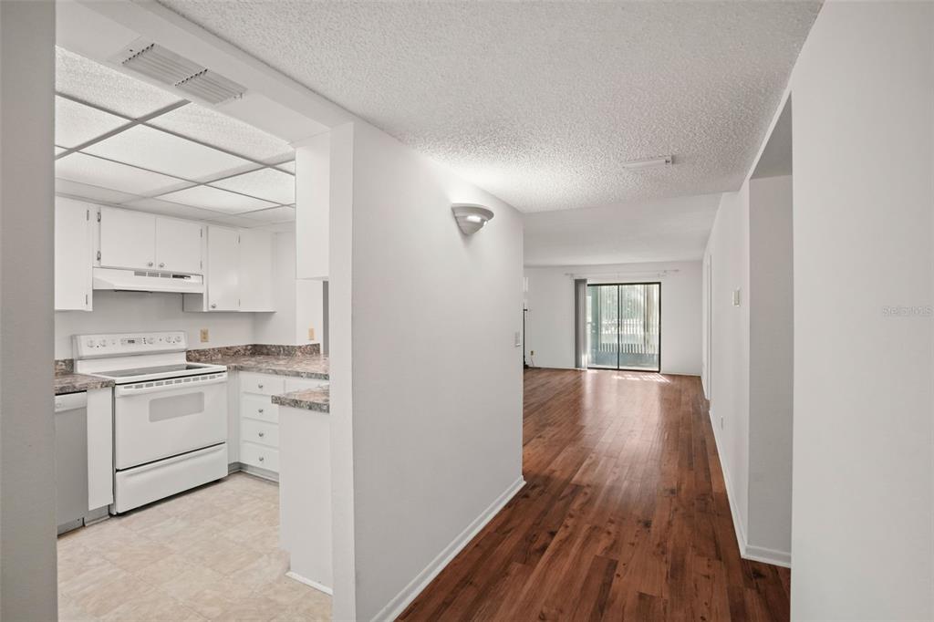 A view from a hallway looking into a white kitchen and a wood-floored living area — 1200 TARPON WOODS BOULEVARD UNIT L4, PALM HARBOR, FL
