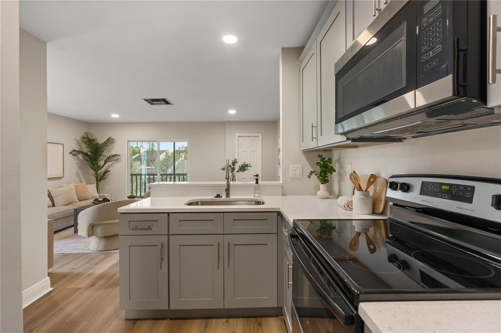 A kitchen with gray cabinets and stainless steel appliances overlooks a living room with balcony — 3848 N LAKE DRIVE UNIT 137, TAMPA, FL