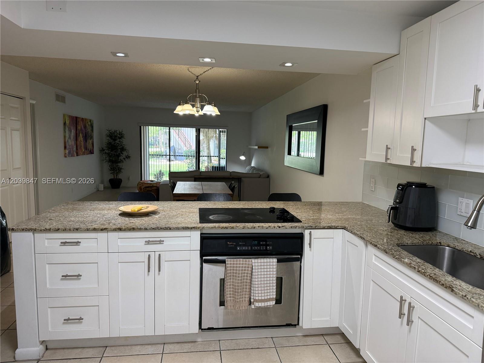 A kitchen with white cabinets and granite countertops overlooks a living and dining area — WESTON, FL
