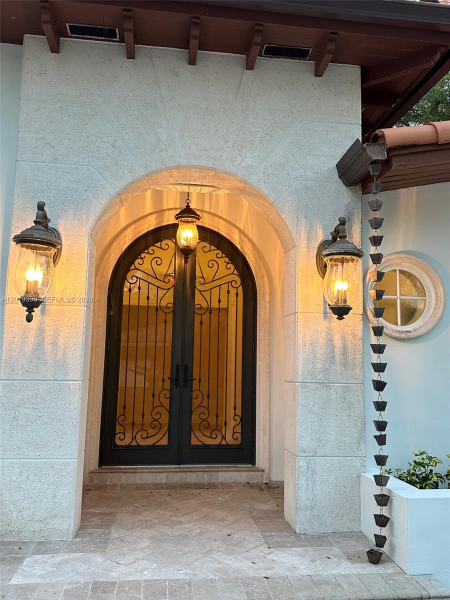 An arched double door with iron scrollwork sits under a covered entryway with wall sconces — 125 W Sunrise Ave, Coral Gables FL 33133, CORAL GABLES, FL