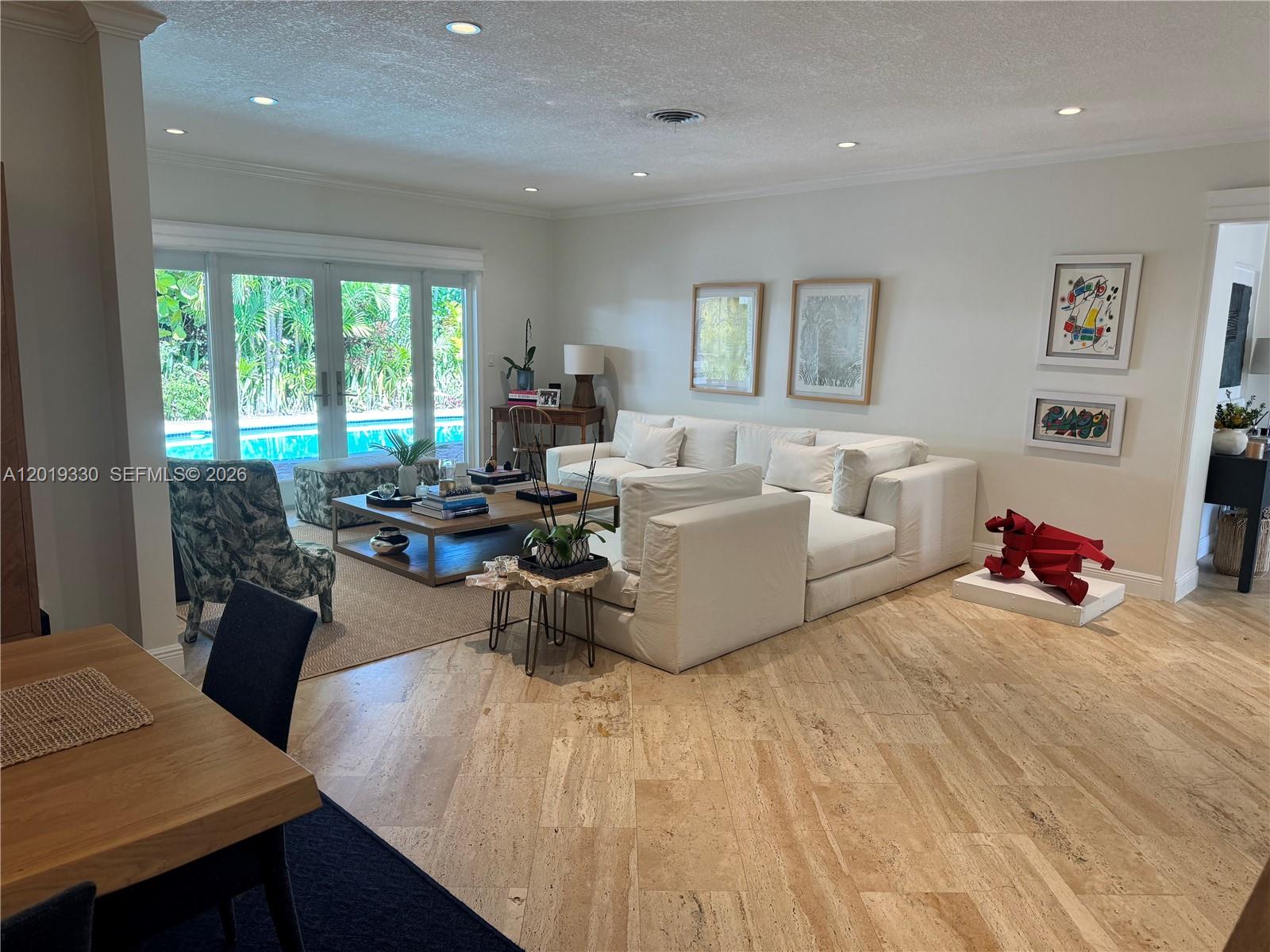 A living room features a white sectional sofa, travertine floors, and views of a pool — 125 W Sunrise Ave, Coral Gables FL 33133, CORAL GABLES, FL