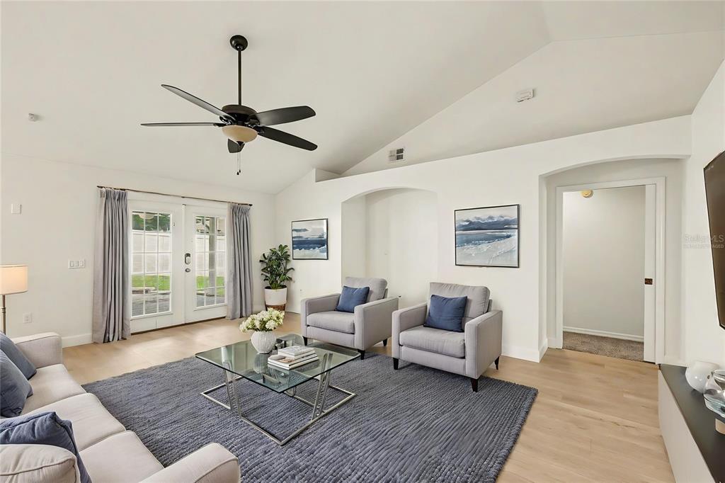 A living room features a vaulted ceiling, a ceiling fan, gray furniture, and glass doors — 7231 REMINGTON OAKS DRIVE, LAKELAND, FL