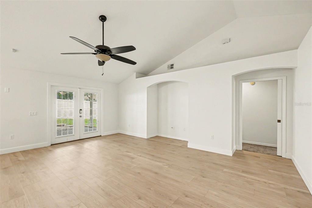 A bright living room features vaulted ceilings, light wood-look flooring, a ceiling fan, and French doors — 7231 REMINGTON OAKS DRIVE, LAKELAND, FL