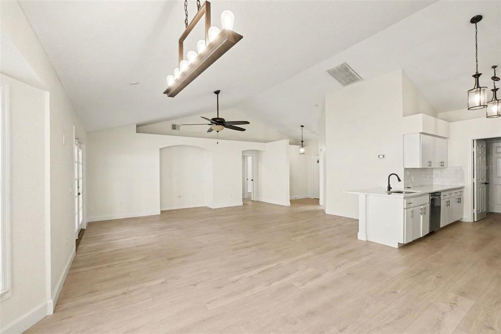 An open-concept living area features light wood flooring, white walls, and a modern kitchen — 7231 REMINGTON OAKS DRIVE, LAKELAND, FL