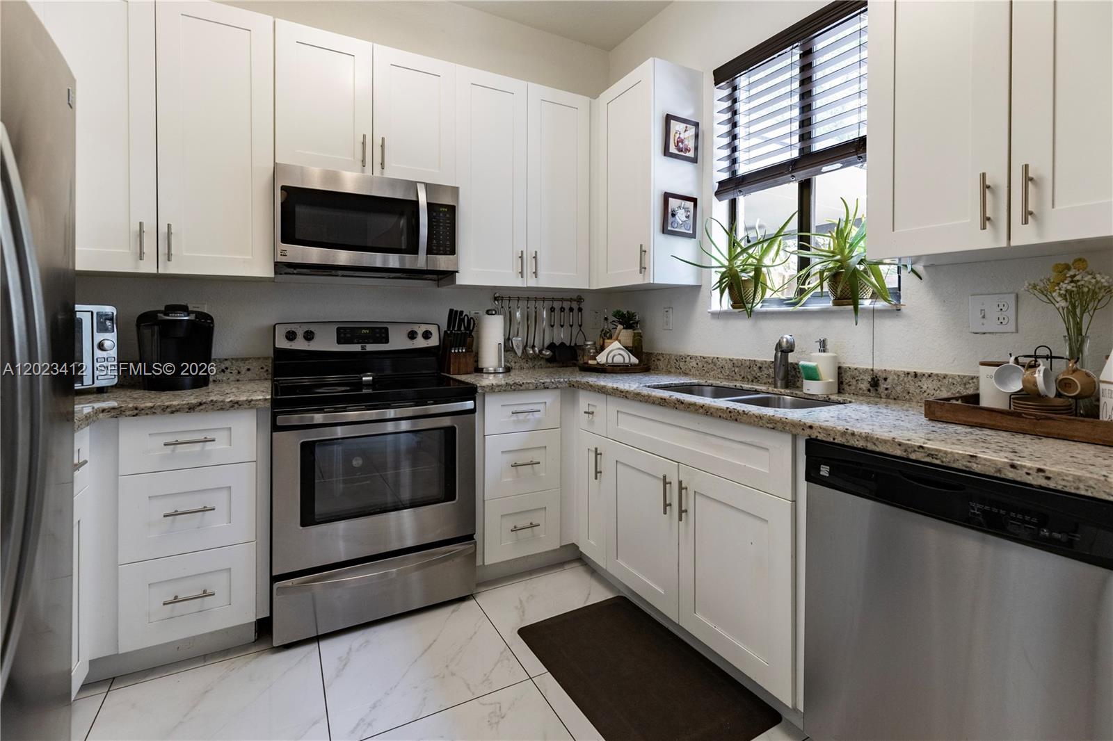 A kitchen features white cabinets, stainless steel appliances, granite countertops, and white marble-look tile flooring — 12704 SW 131st Ter, Miami FL 33186, MIAMI, FL