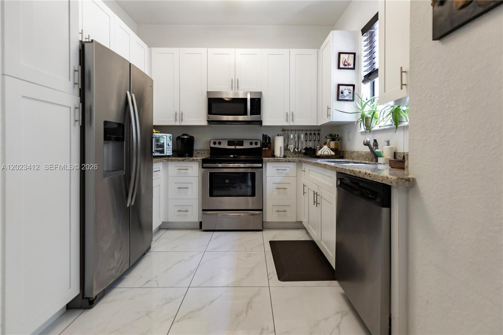 A galley kitchen features white cabinets, stainless steel appliances, and marble-look tile flooring — 12704 SW 131st Ter, Miami FL 33186, MIAMI, FL