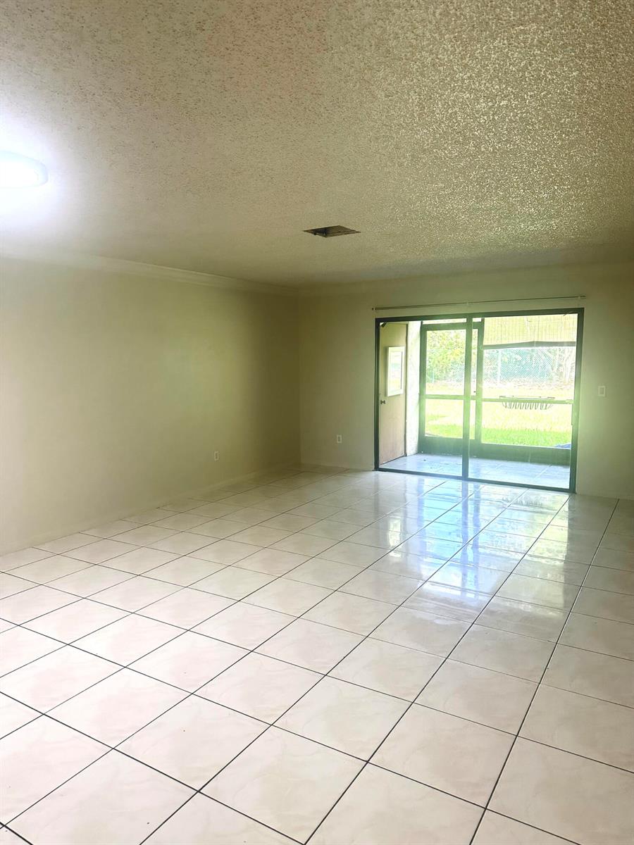 An empty room with light-colored tile flooring, beige walls, and a sliding glass door — 405 Lakeview Drive E, Royal Palm Beach FL 33411, ROYAL PALM BEACH, FL