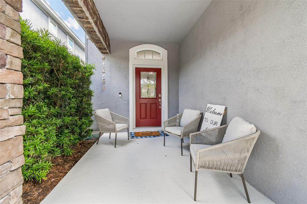 A covered front porch features a red door, three chairs, and a welcome sign — 16214 BAYBERRY VIEW DRIVE, LITHIA, FL