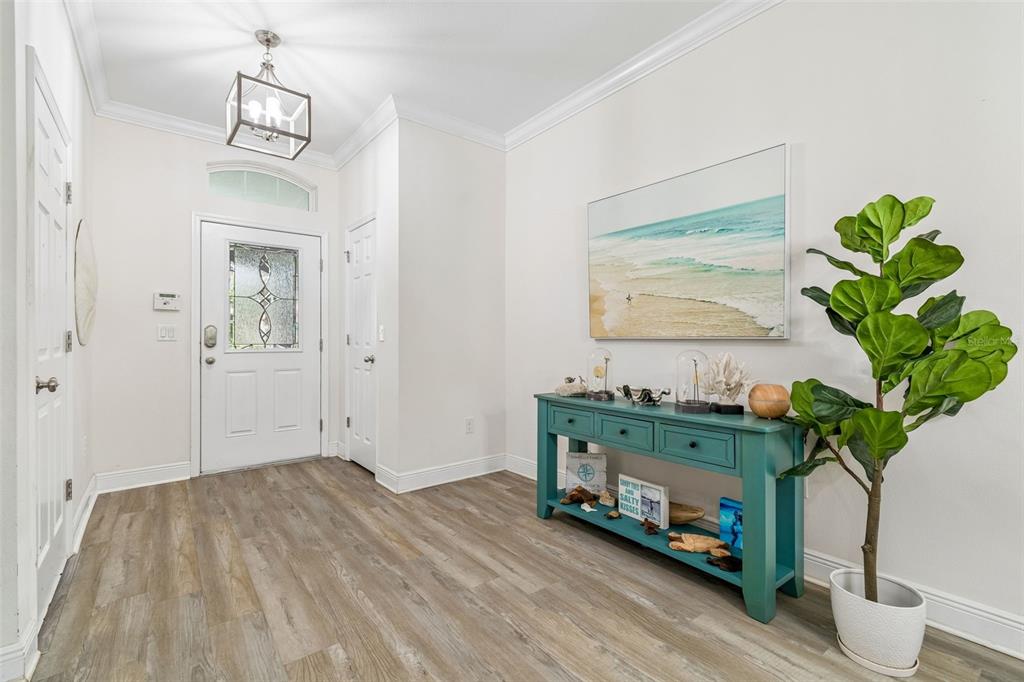 An entryway features light wood-look flooring, a teal console table, and a large beach painting — 16214 BAYBERRY VIEW DRIVE, LITHIA, FL