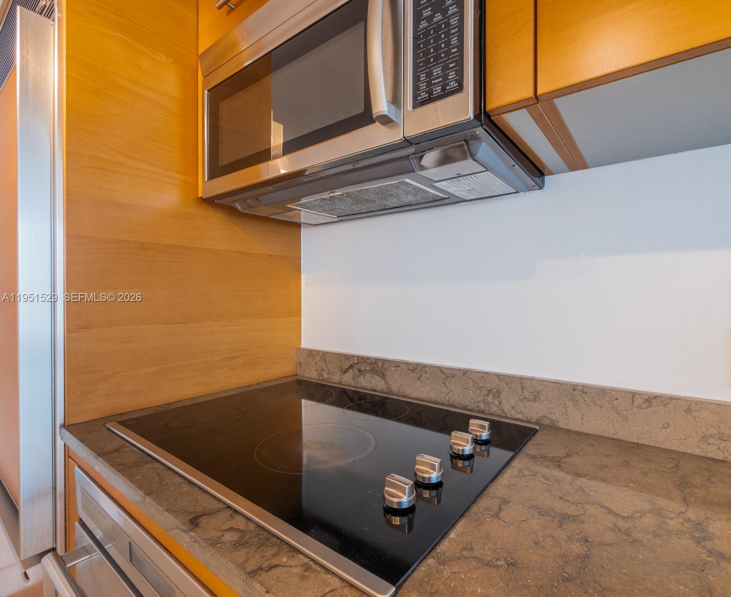 A kitchen features a black glass cooktop, stainless steel microwave, and wood-toned cabinetry — 465 Brickell Ave # 2304, Miami FL 33131, MIAMI, FL