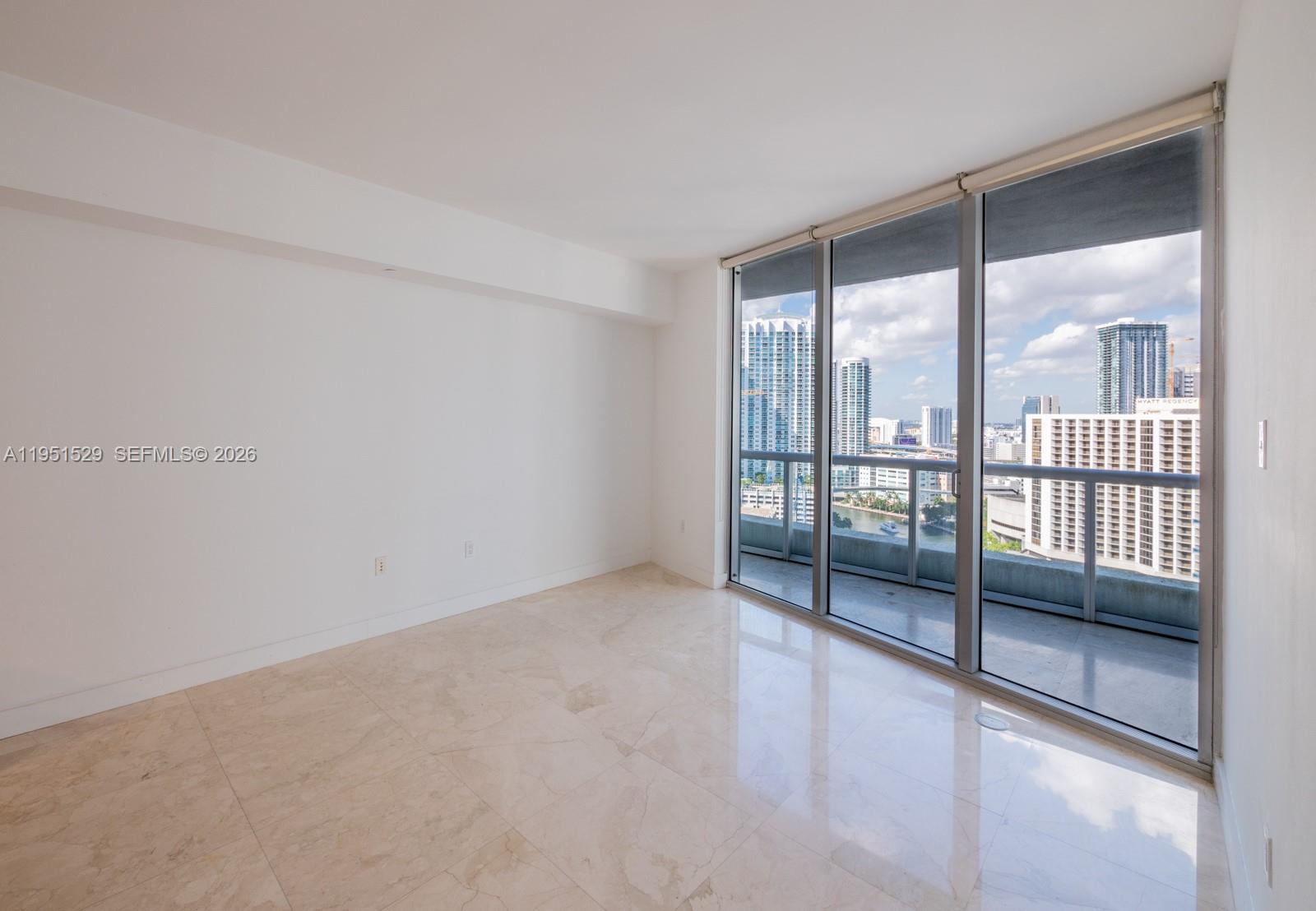 An empty room with marble floors features floor-to-ceiling windows overlooking a city skyline — 465 Brickell Ave # 2304, Miami FL 33131, MIAMI, FL