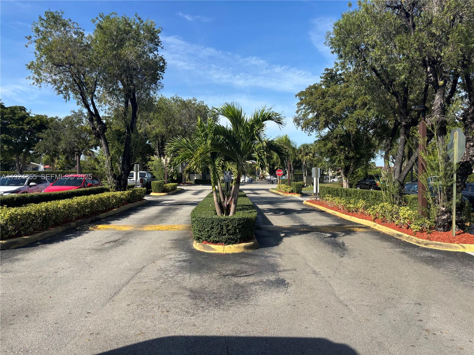 A paved driveway with a central palm tree island leads toward a gated entrance — 14250 SW 62nd St # 520, Miami FL 33183, MIAMI, FL