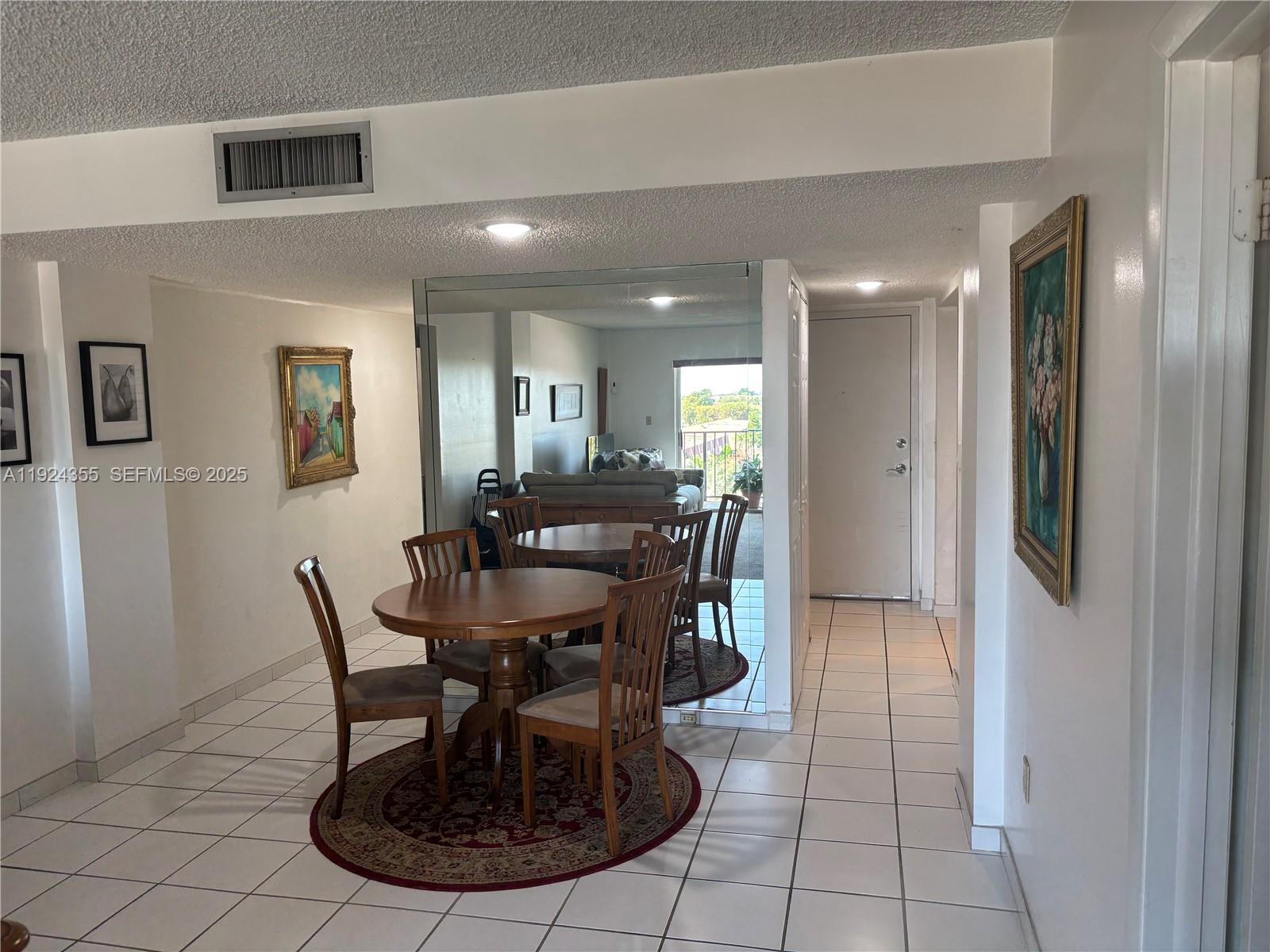 A dining area with a round wooden table, chairs, and a large mirrored wall — 14250 SW 62nd St # 520, Miami FL 33183, MIAMI, FL