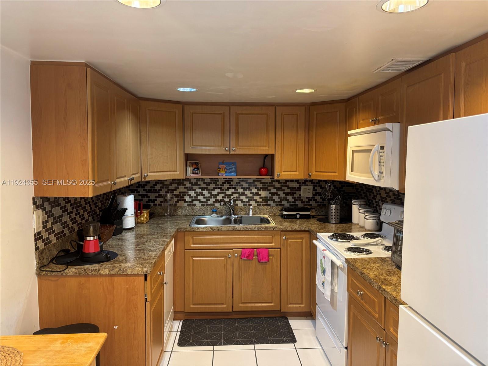 A kitchen features wood cabinets, a mosaic tile backsplash, laminate countertops, and white appliances — 14250 SW 62nd St # 520, Miami FL 33183, MIAMI, FL