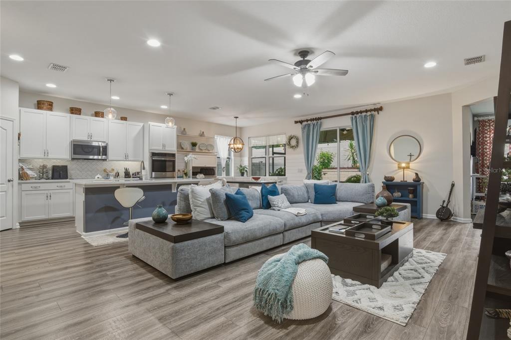 An open-concept living room and kitchen featuring a large gray sectional, wood flooring, and cabinetry — 16742 ABBEY HILL COURT, CLERMONT, FL