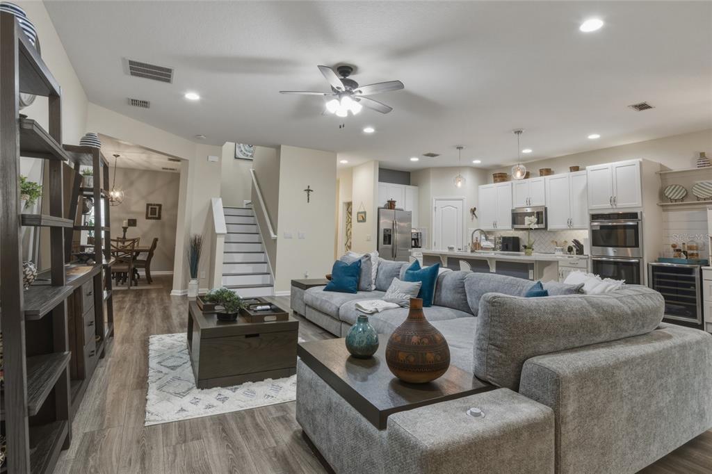 An open-concept living room features a large gray sectional, wood-look flooring, and a kitchen area — 16742 ABBEY HILL COURT, CLERMONT, FL