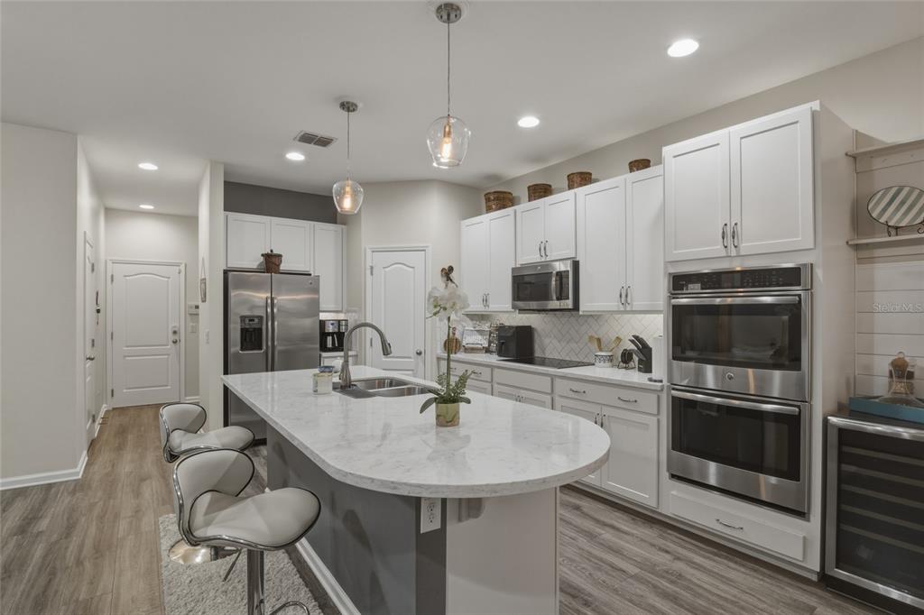 A modern kitchen features white cabinetry, a large marble-topped island, and stainless steel appliances — 16742 ABBEY HILL COURT, CLERMONT, FL