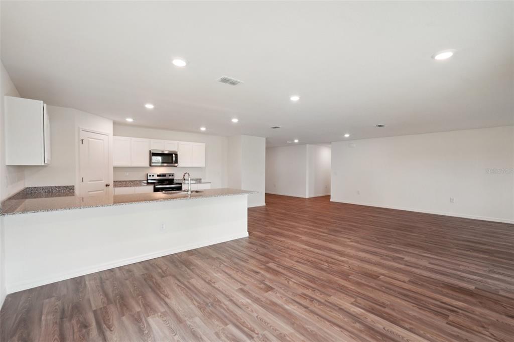 An open-concept kitchen with white cabinets and granite countertops overlooks a large living area — 13 FRINGETREE STREET, HOMOSASSA, FL